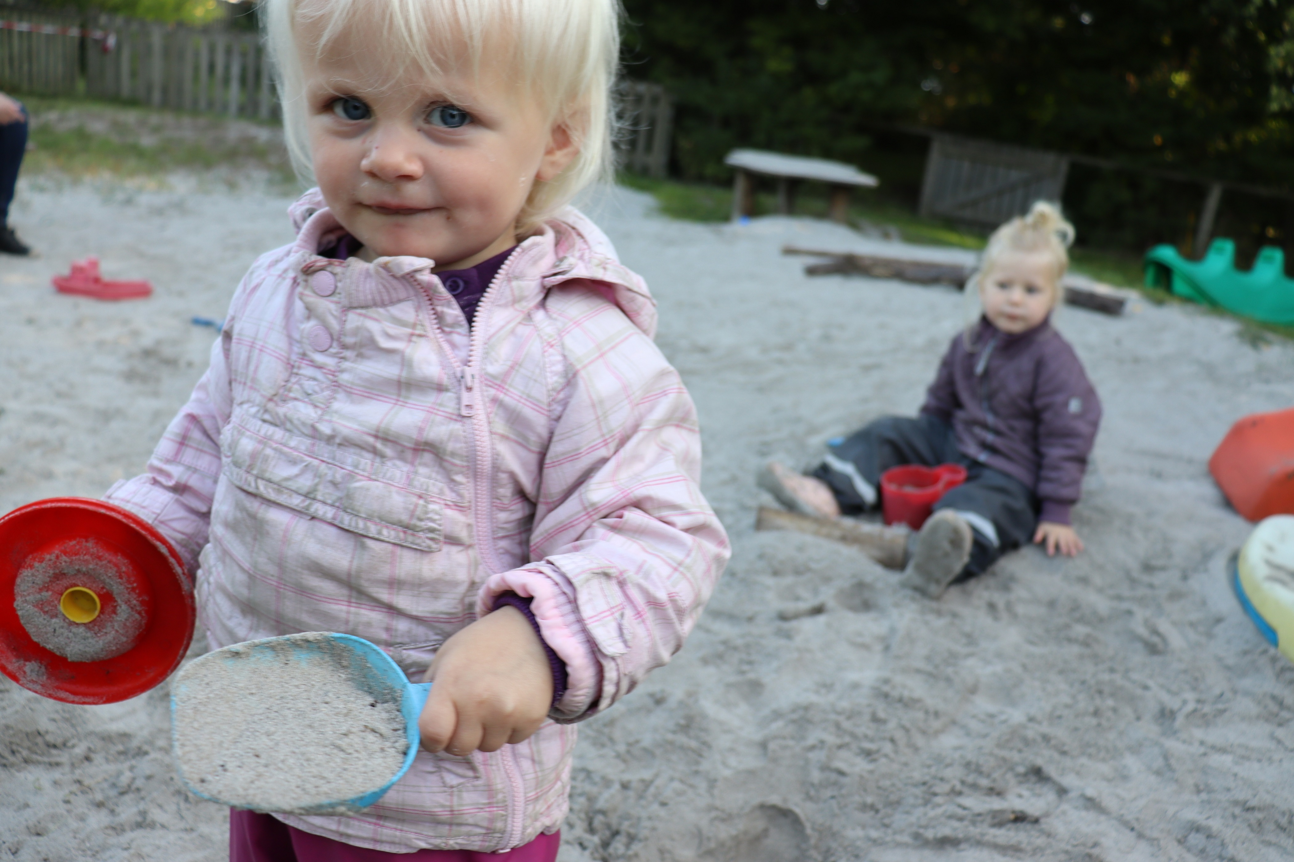 Vuggestuens legeplads, hvor en lille pige står med sandkasse skovl og gryde