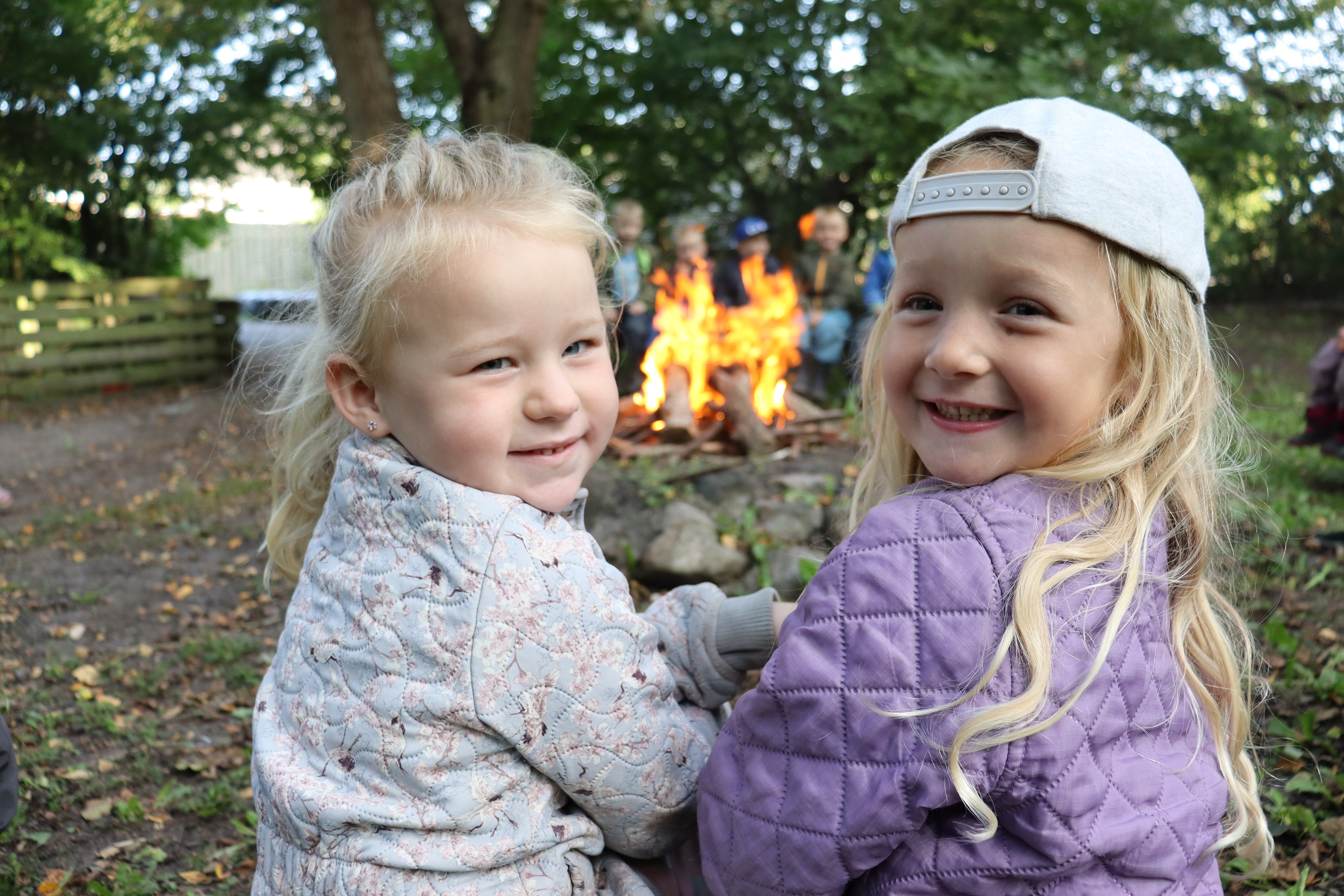 To piger sidder ved bål og kigger bagud til kameraet